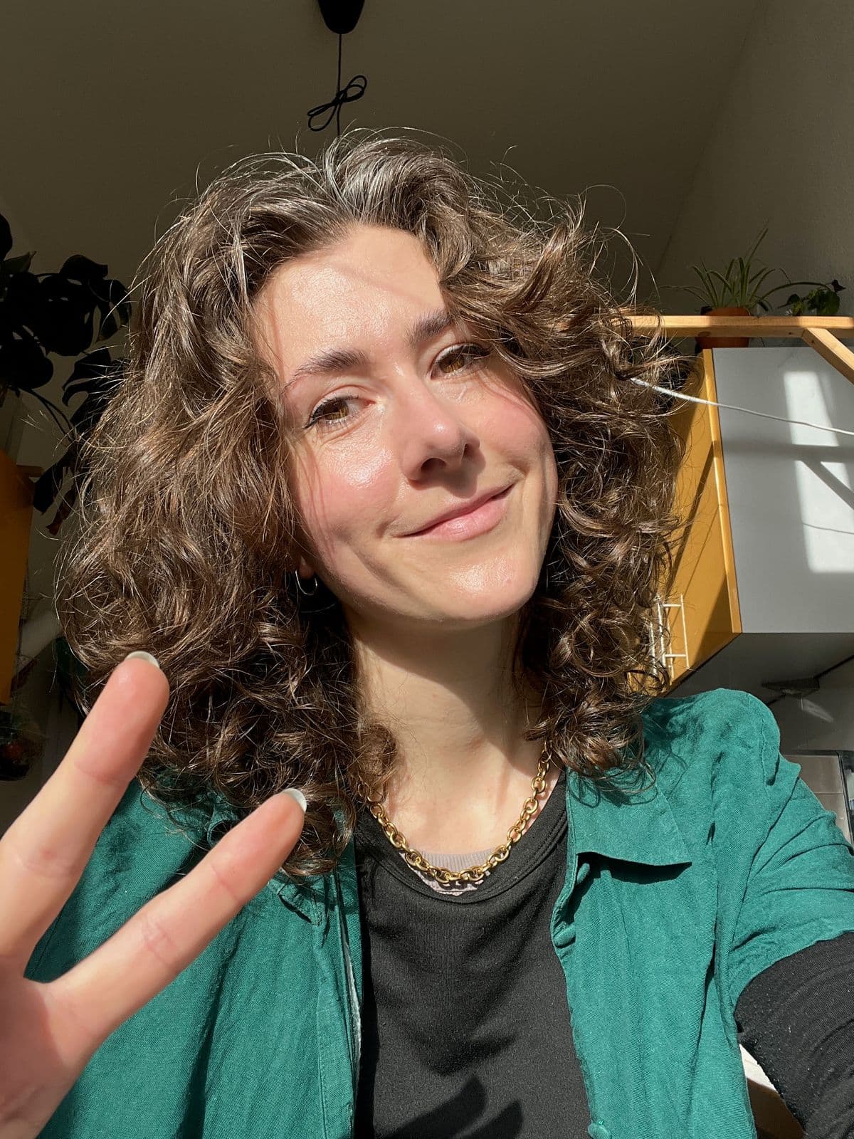 Close‑up portrait of Clara smiling in warm daylight, holding up a peace sign.