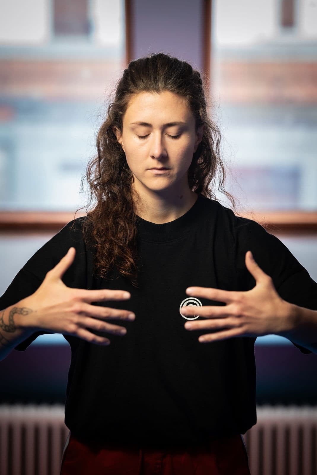 Clara standing in a qi gong pose with eyes closed and both hands resting on her chest, in soft natural light.