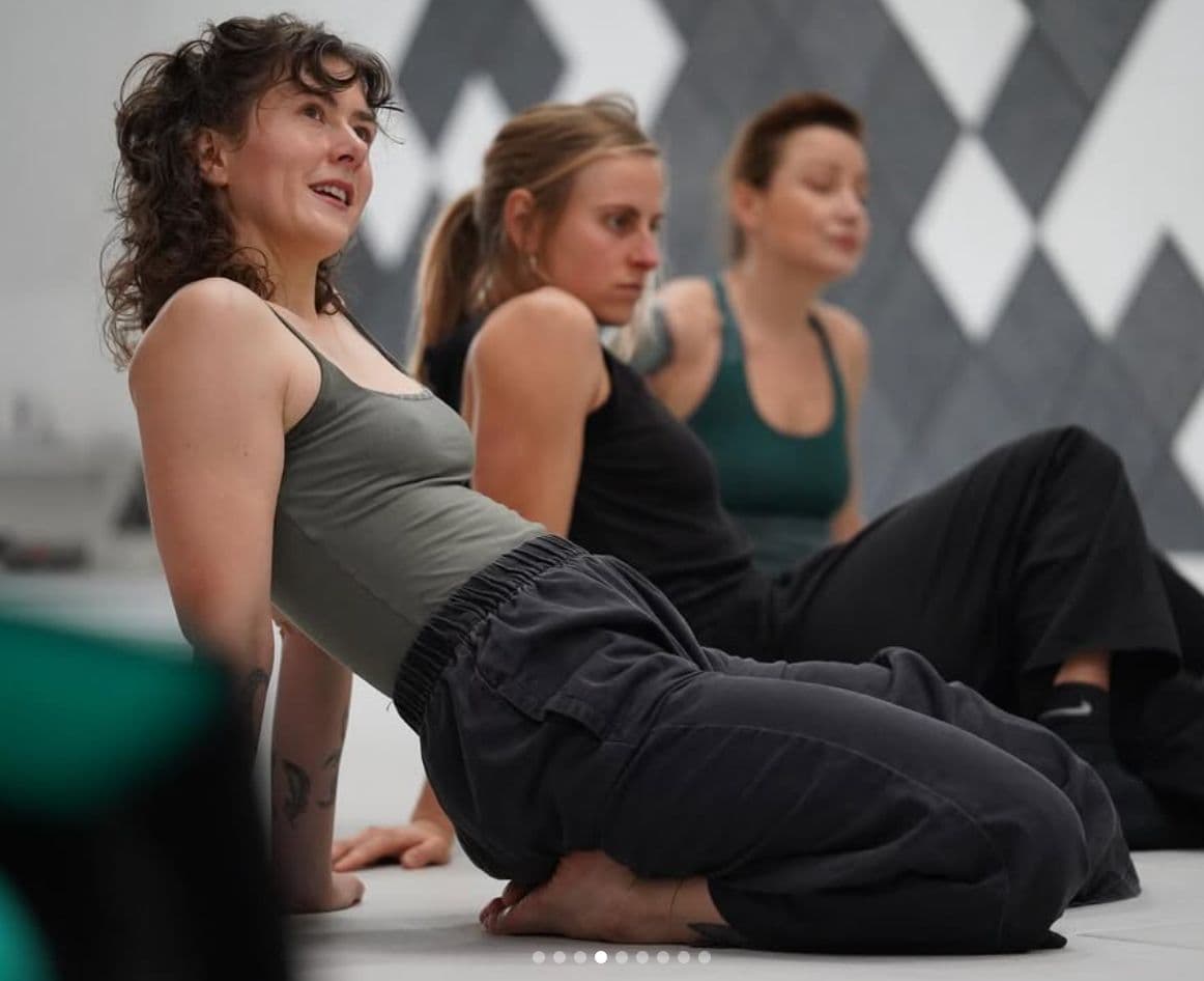 Clara seated on the floor mid-conversation with several students during a group movement class.